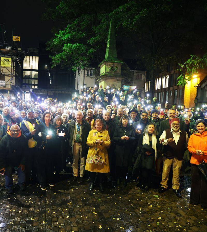 People holding candles and phone lights at a vigil.